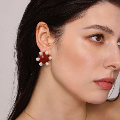Woman wearing angry statement gold stud earrings with red center and pearl accents