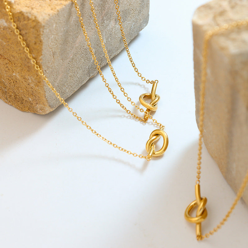 Gold unique heart knot pendant jewelry necklace displayed on white surface with stone blocks