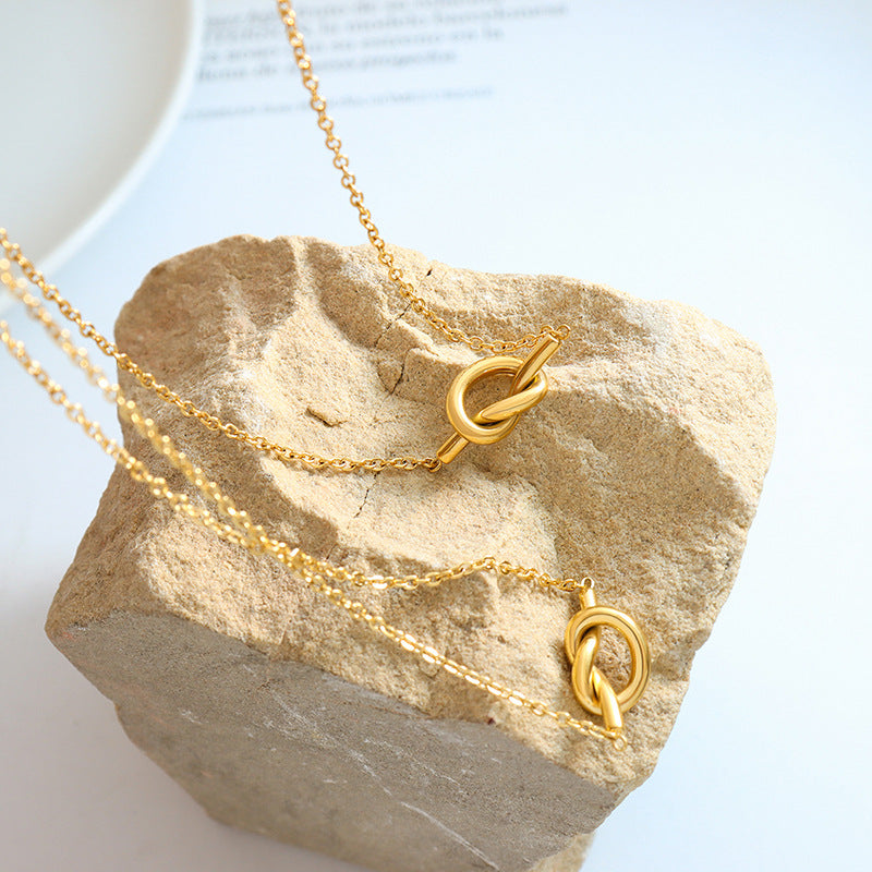 Gold unique heart knot pendant jewelry necklace set displayed on textured stone background