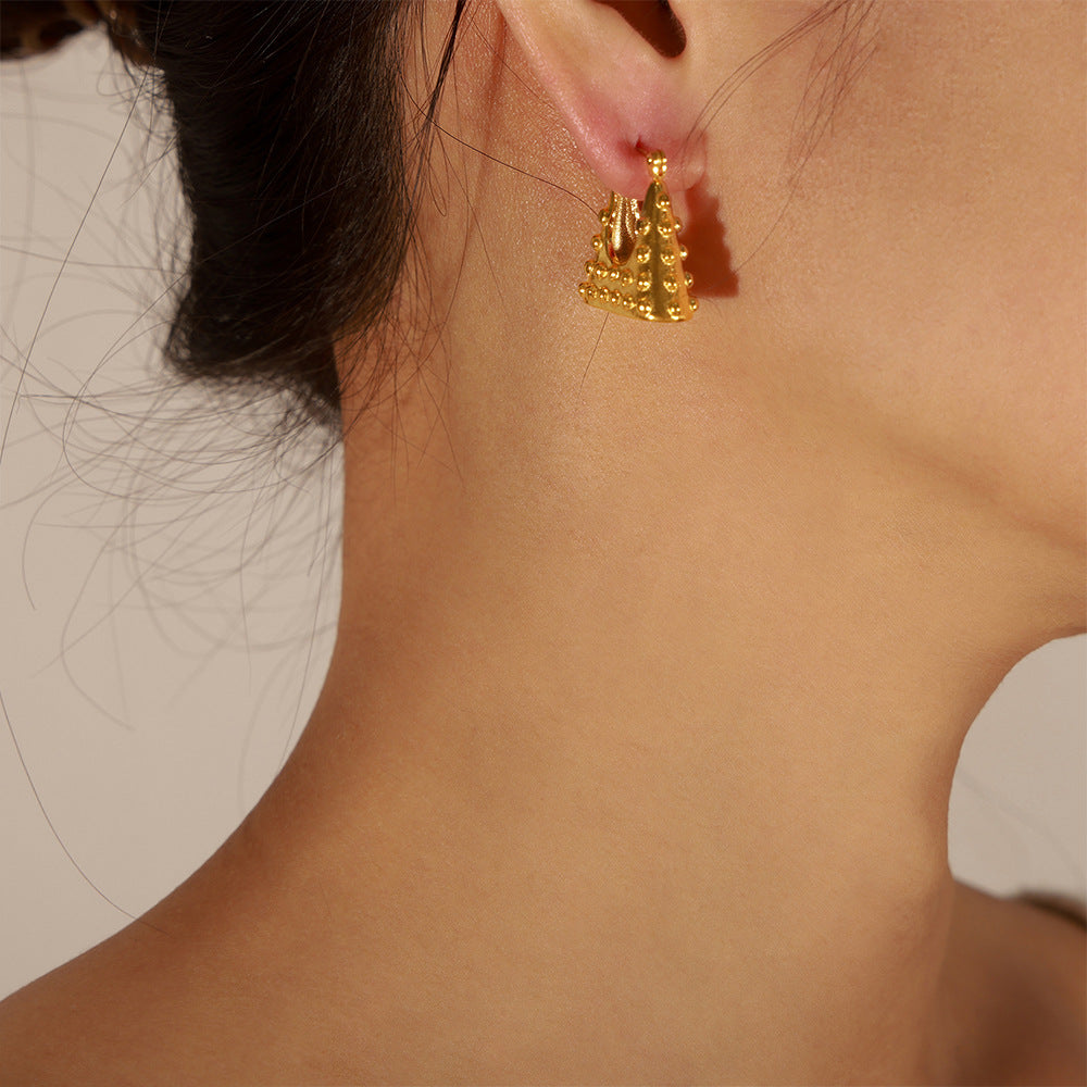 Close-up of a woman wearing geometric gold earrings with textured pyramid design