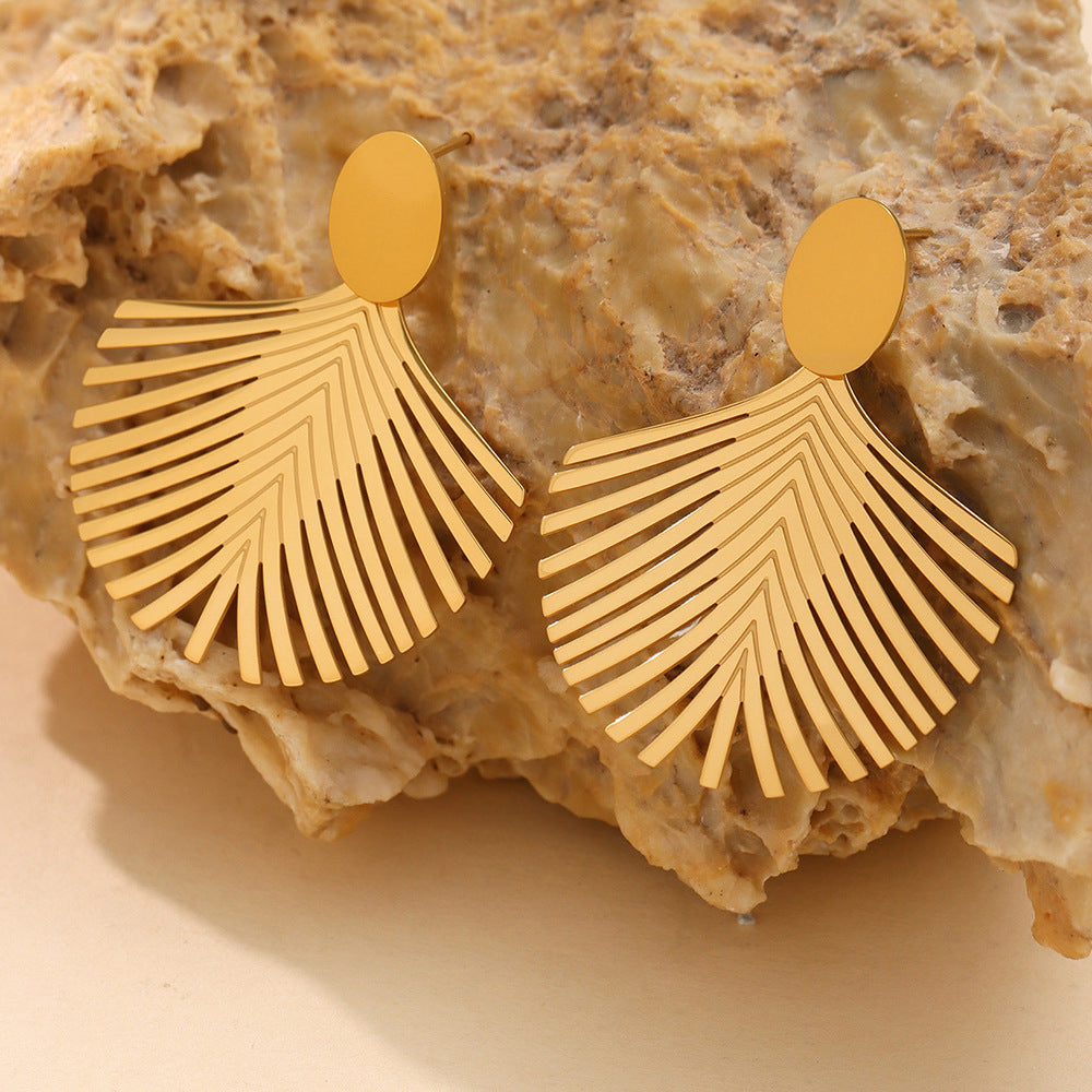 Gold palm leaf earrings with a textured design displayed on a natural stone background