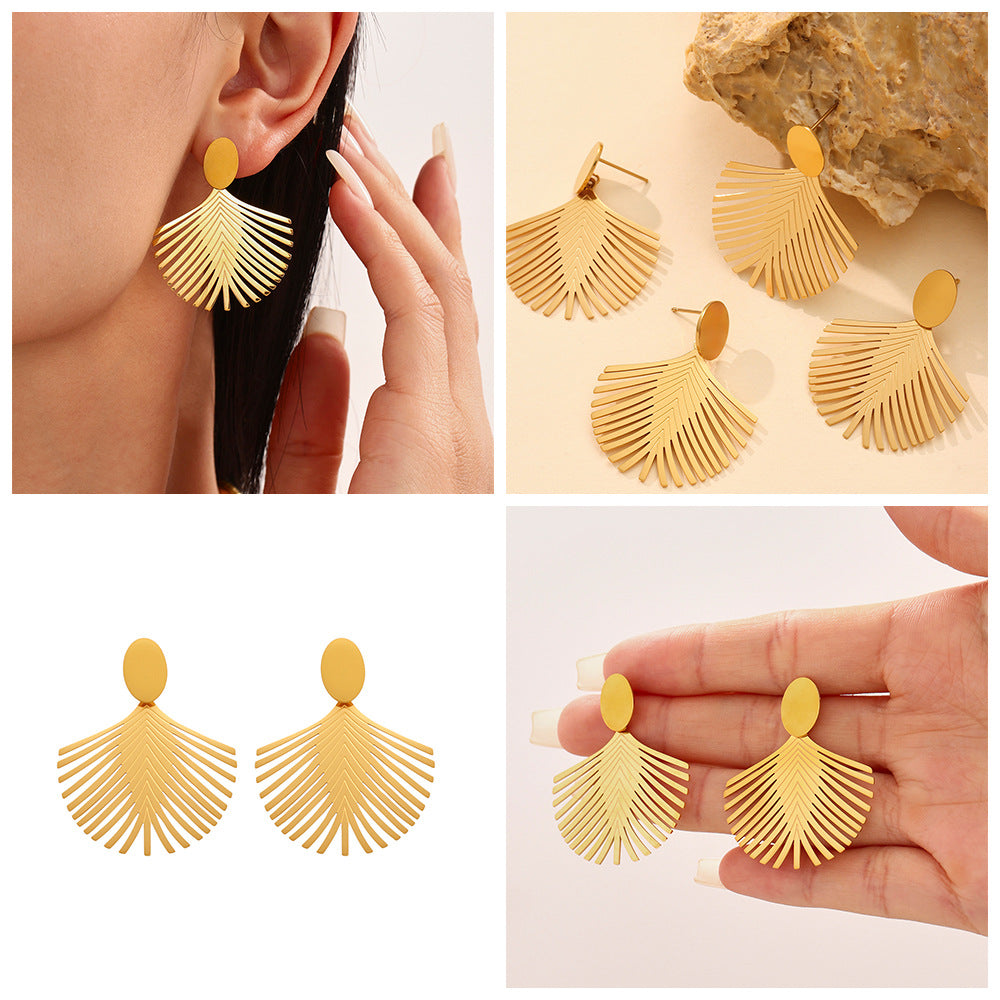 Gold palm leaf earrings shown on ear and held in hand with detailed leaf design