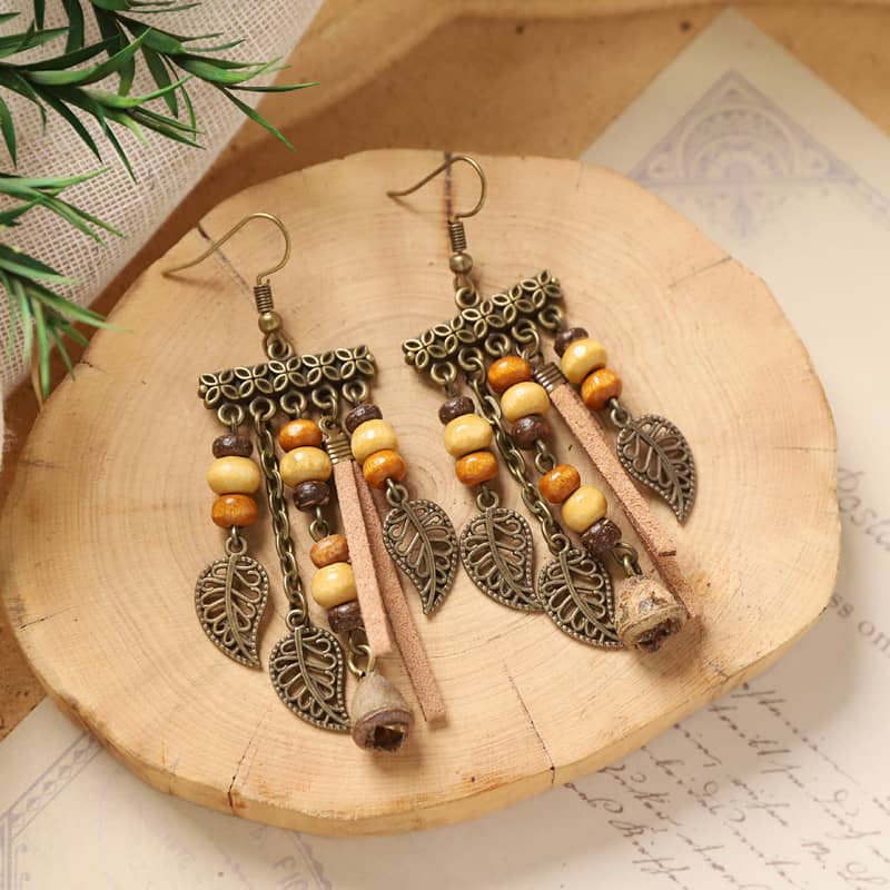 Vintage leaf tassel earrings with colorful beads and a bohemian design on a wooden plate