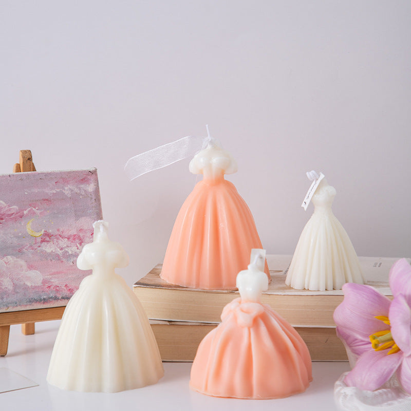 Set of four wedding dress candle decorations in white and peach colors displayed on books and near a flower