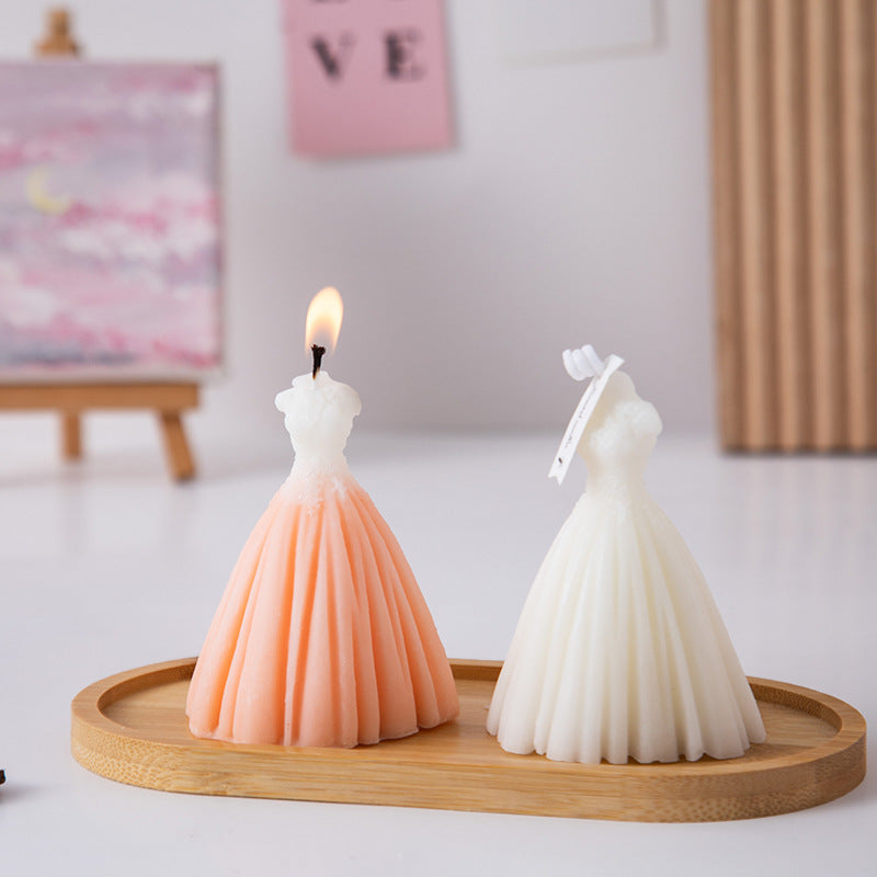 Two wedding dress candle designs in white and peach on a wooden tray with one candle lit
