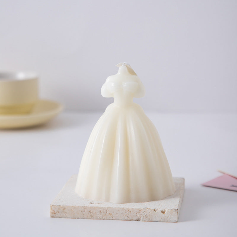 White wedding dress candle shaped like a bridal gown displayed on a stone tile