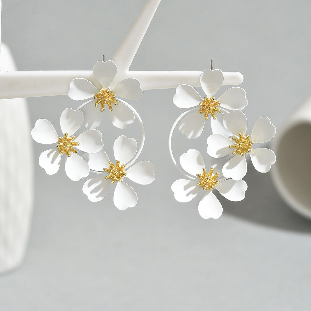 White sunflower earrings with delicate white petals and gold centers hanging on a display stand