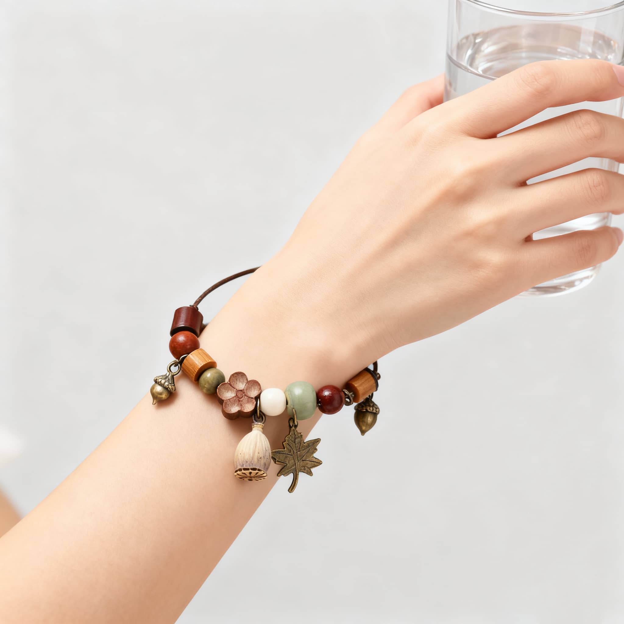 Wood bead mindfulness bracelet with natural elements and a decorative charm, worn on a hand near a glass of water.